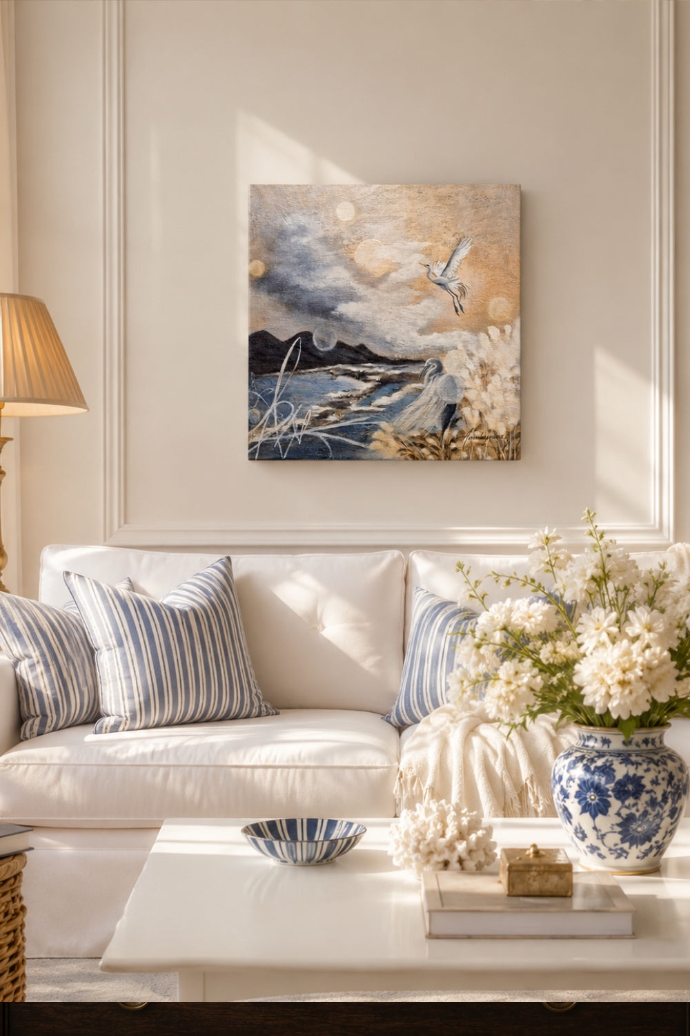 "New Horizons Ahead" by Annika Andersson — original painting displayed above a white sofa in a bright Scandinavian-style living room with blue and white striped cushions and a bouquet of white flowers